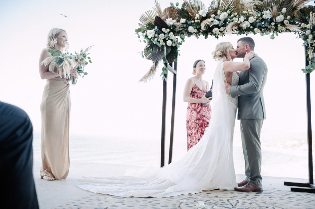 Bride and groom first kiss at Villa Amor Sayulita beach wedding ceremony under floral arch