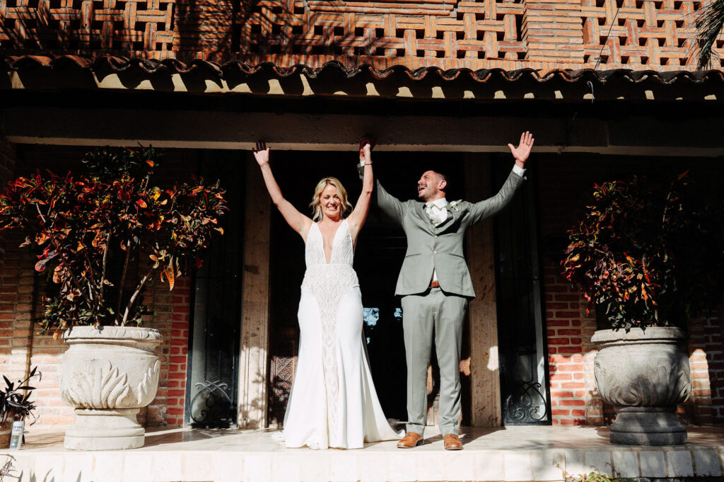 Bride and groom raising hands in celebration at Villa Amor Sayulita wedding ceremony, brick hacienda backdrop