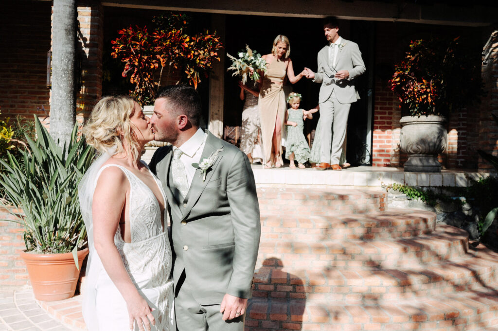 Bride and groom share first kiss at Villa Amor Sayulita wedding ceremony with bridal party on steps