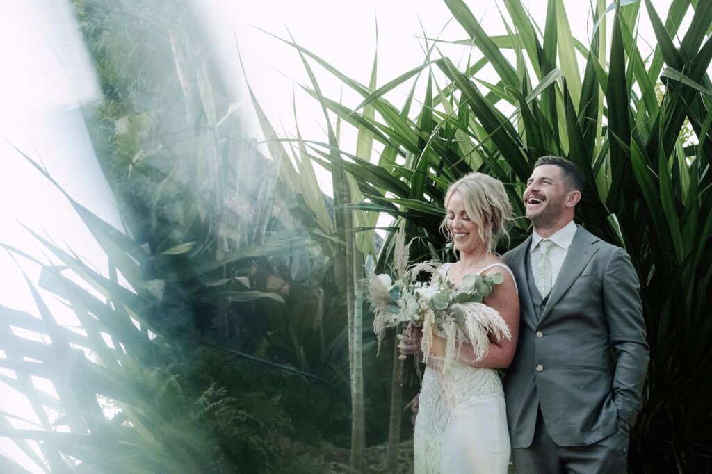 Bride and groom laughing among tropical palms at Villa Amor Sayulita wedding, bouquet of pampas and eucalyptus