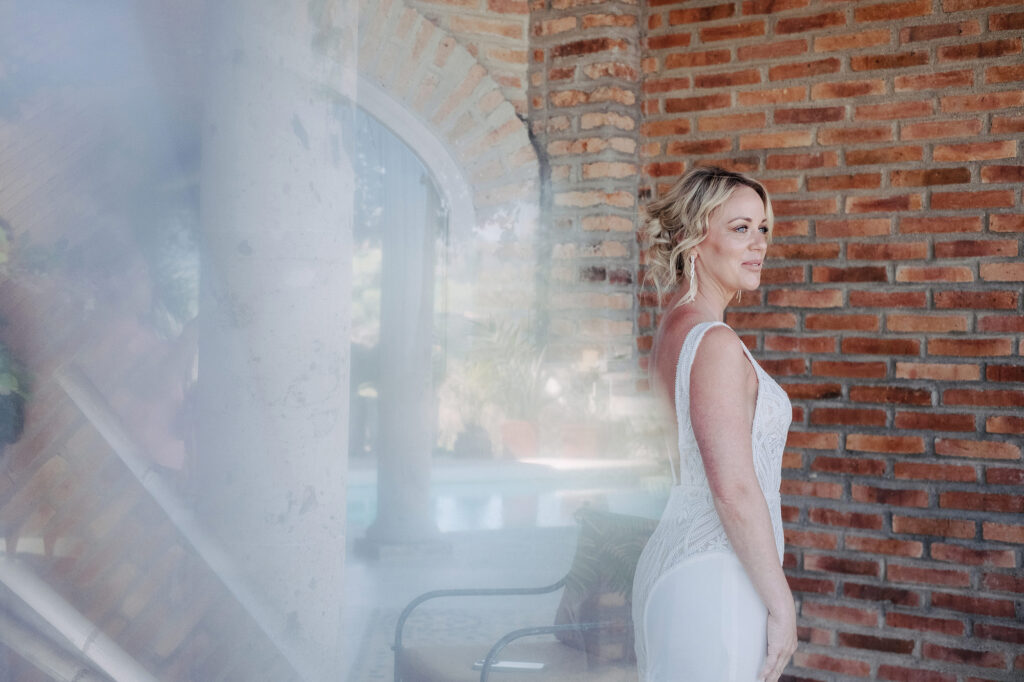 Bride in white gown at Villa Amor Sayulita, standing by brick archway, documentary wedding photo