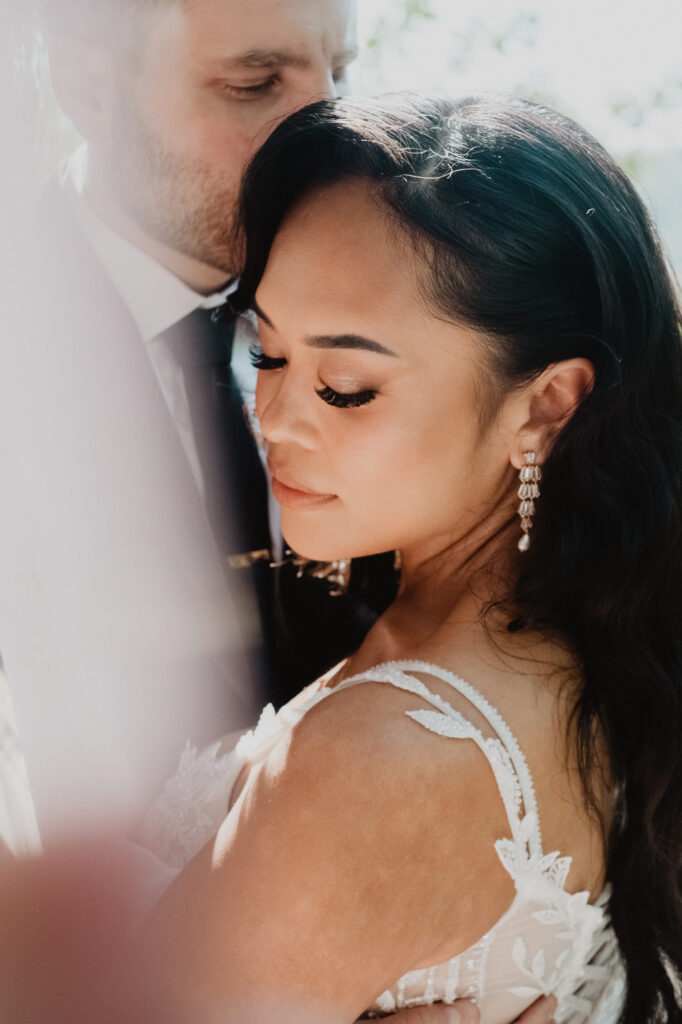 Bride in lace gown with chandelier earrings, groom kissing her head, Villa Valentin Sayulita wedding