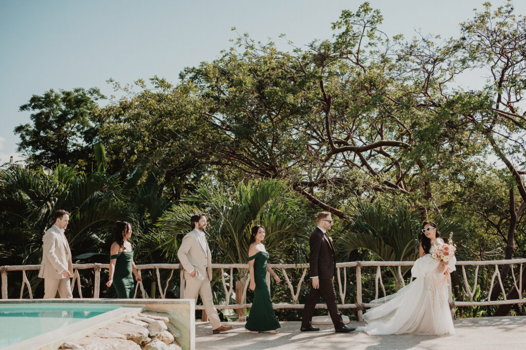 Wedding party walking poolside at Villa Valentin Sayulita, bride in white gown with bouquet, green bridesmaids dresses