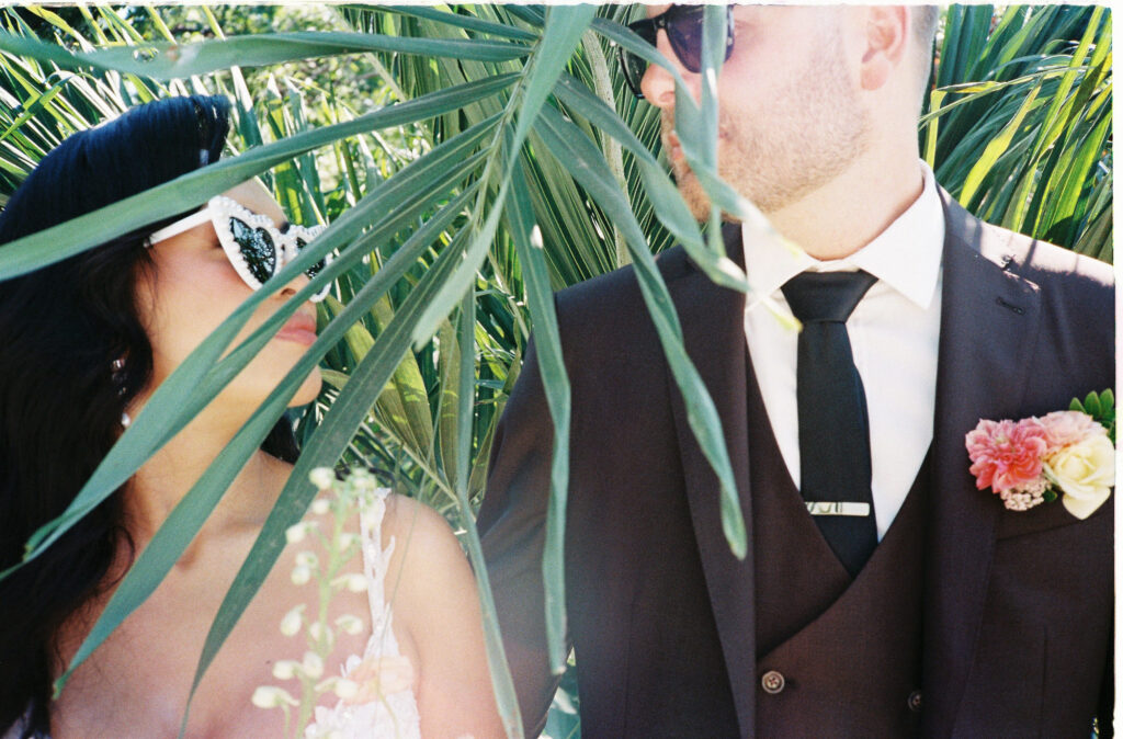 Bride and groom peek through tropical palm fronds at Villa Valentin Sayulita wedding, analog film photo