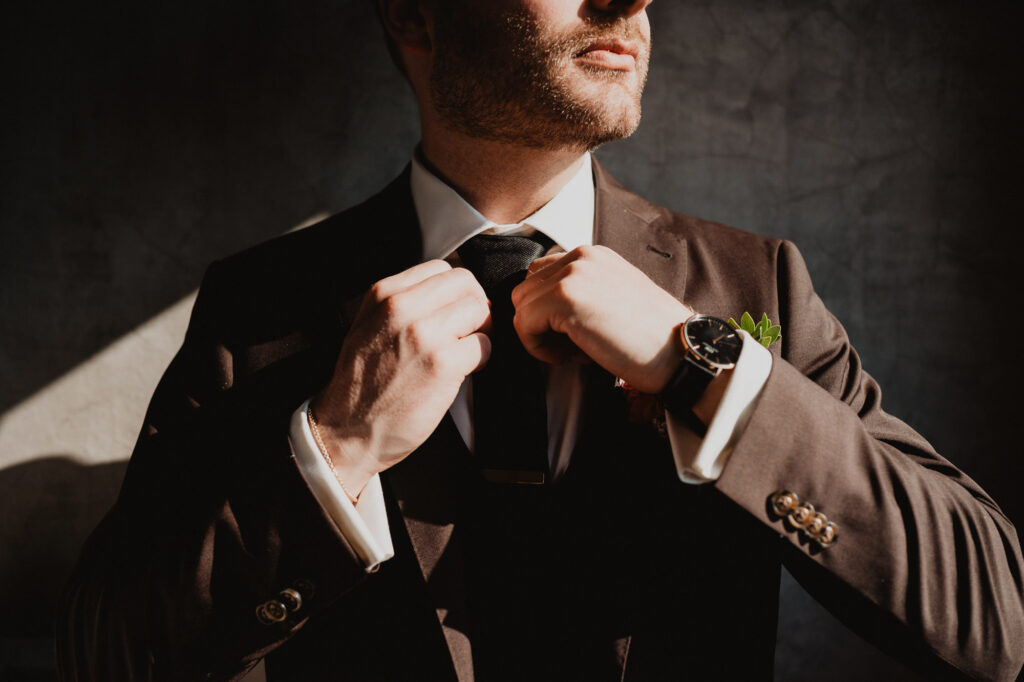 Groom adjusting tie in charcoal suit with boutonniere, wedding day preparation at Villa Valentin Sayulita