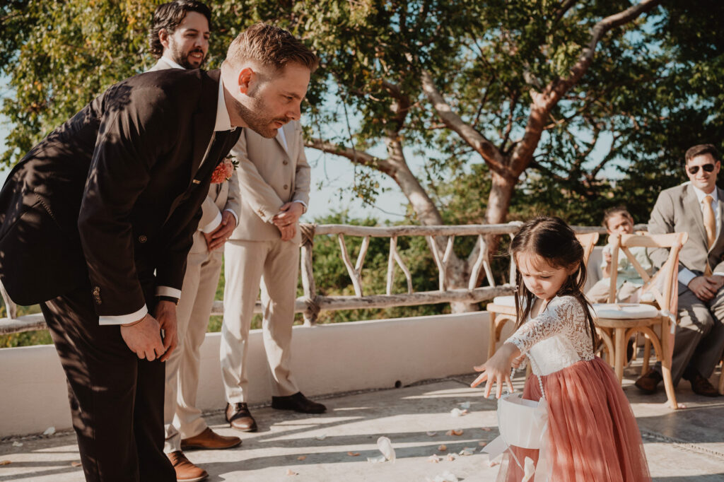 Groom bends down to greet flower girl scattering petals at Villa Valentin wedding ceremony, Sayulita