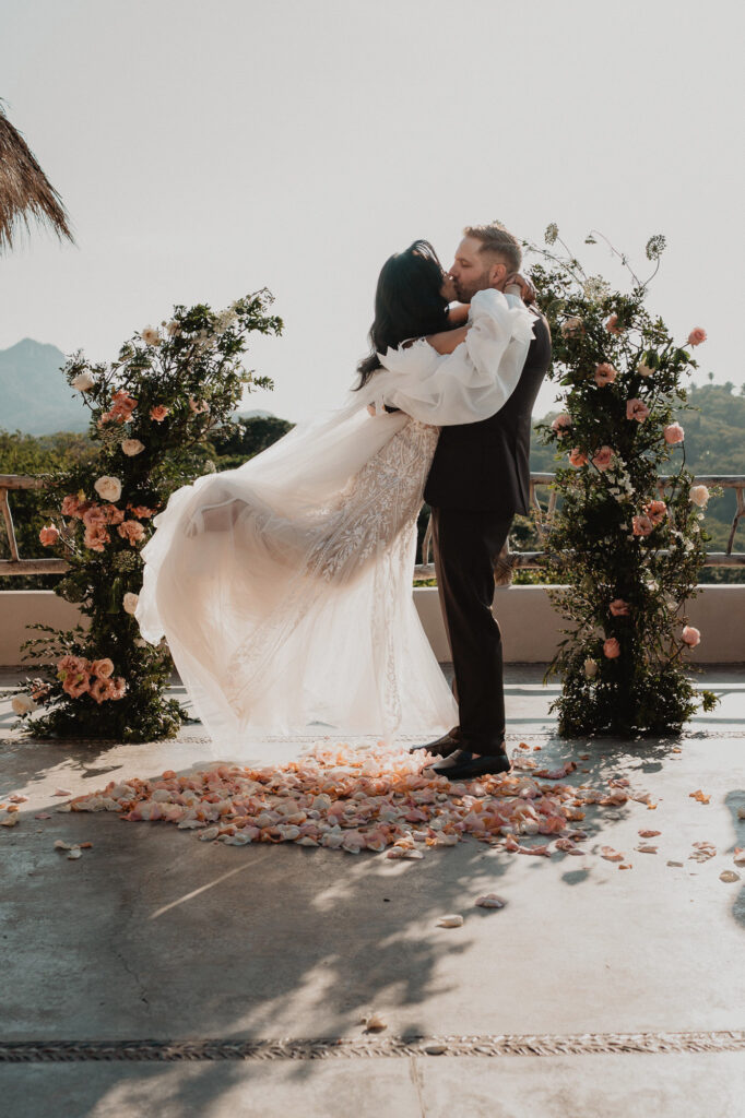 Groom lifts bride during first kiss at Villa Valentin wedding ceremony, Sayulita, surrounded by floral arches