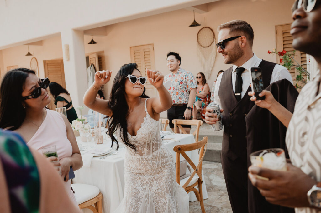 Bride dancing in lace gown and heart sunglasses at outdoor wedding reception, Villa Valentin Sayulita