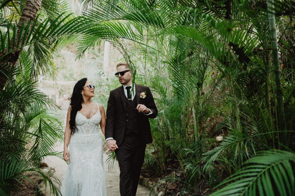 Bride and groom walking hand in hand through tropical palms at Villa Valentin, Sayulita wedding