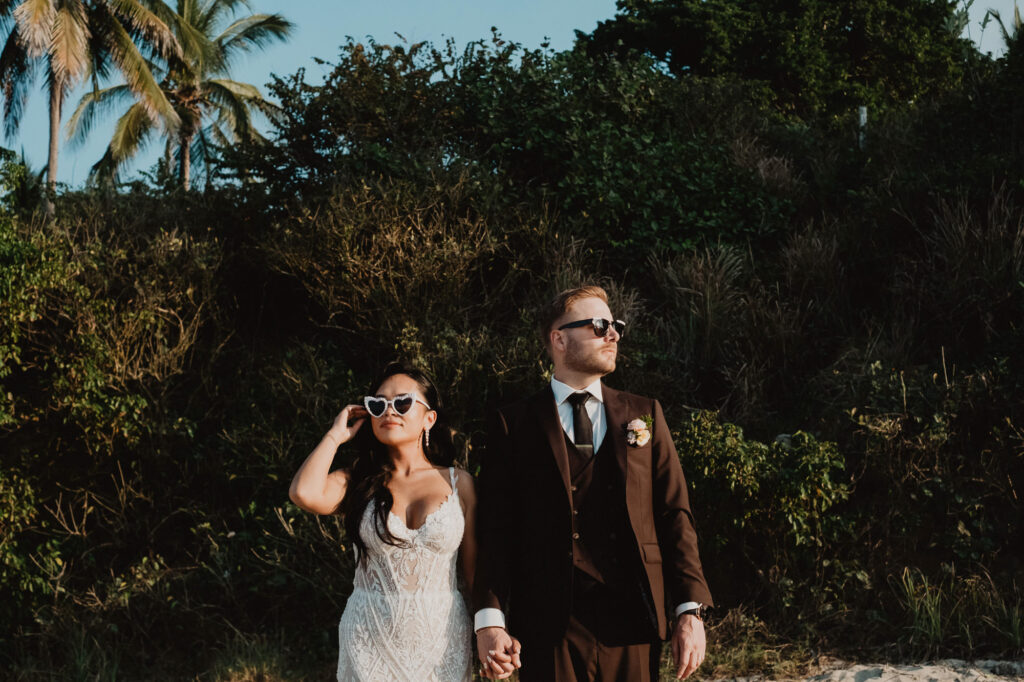 Bride and groom holding hands in sunglasses at Villa Valentin Sayulita wedding, lush tropical greenery background