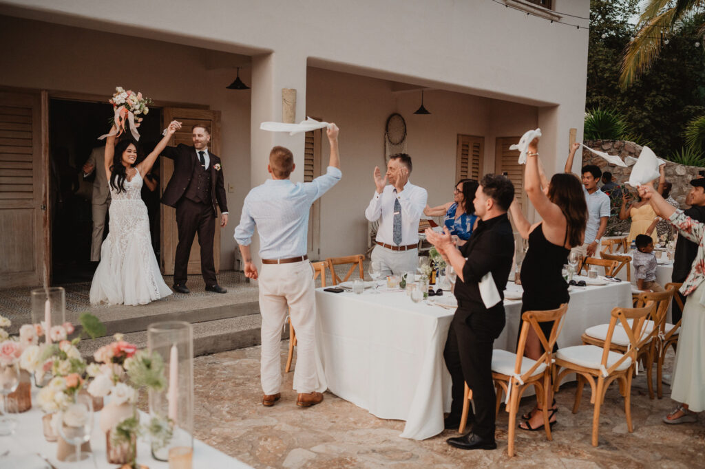 Bride and groom grand entrance at Villa Valentin Sayulita wedding reception, guests waving napkins in celebration