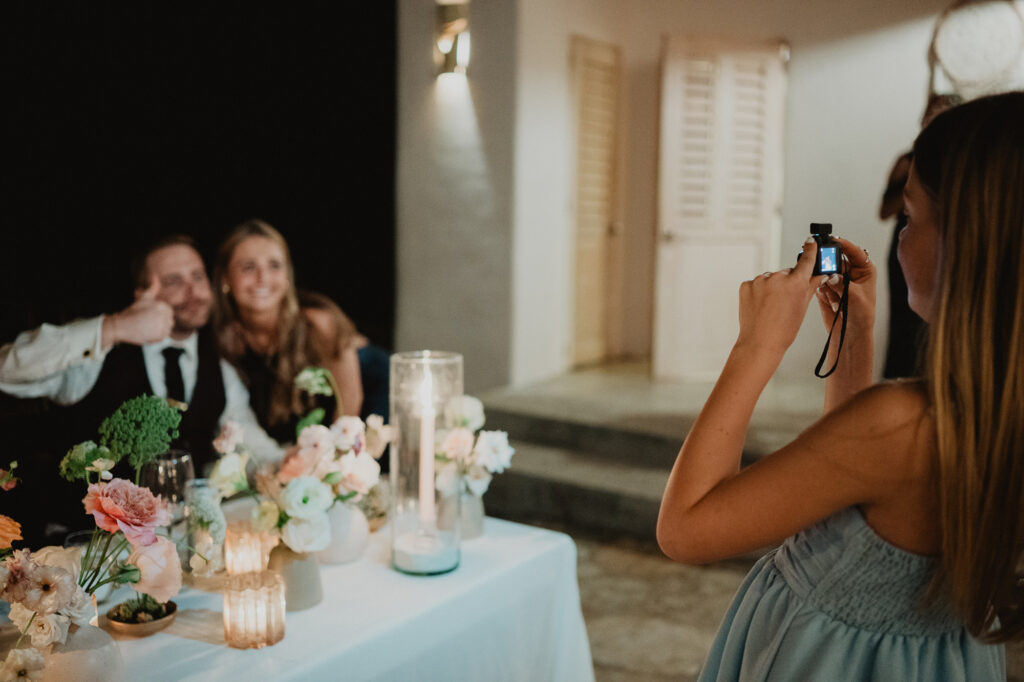 Wedding guest photographing couple at sweetheart table with floral centerpieces, Villa Valentin Sayulita reception