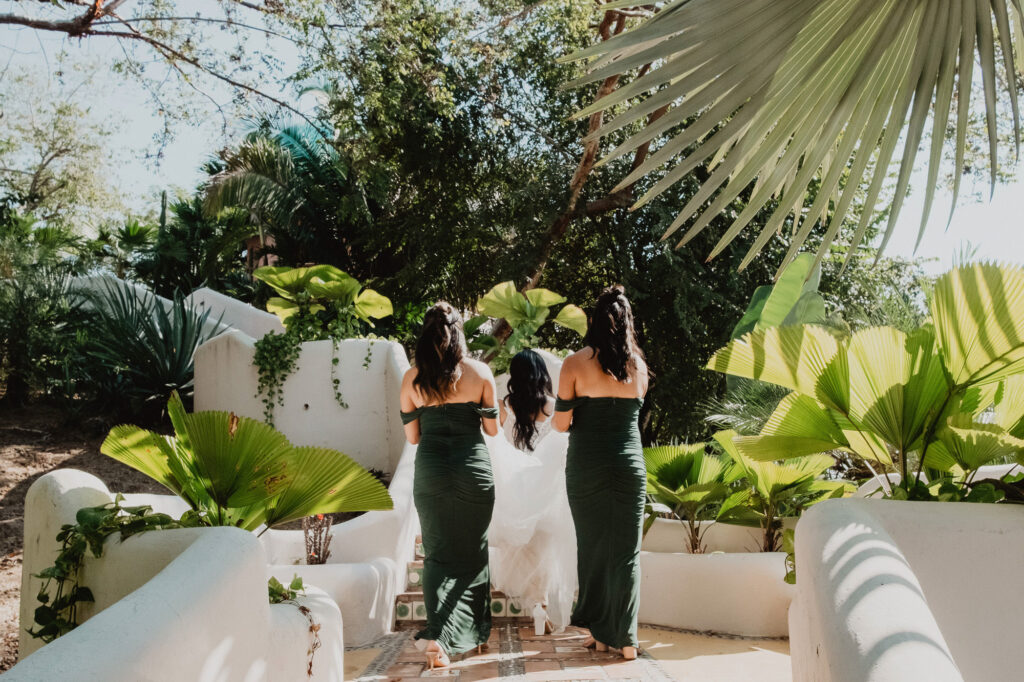 Bridesmaids in forest green gowns walk with bride through tropical garden at Villa Valentin Sayulita wedding