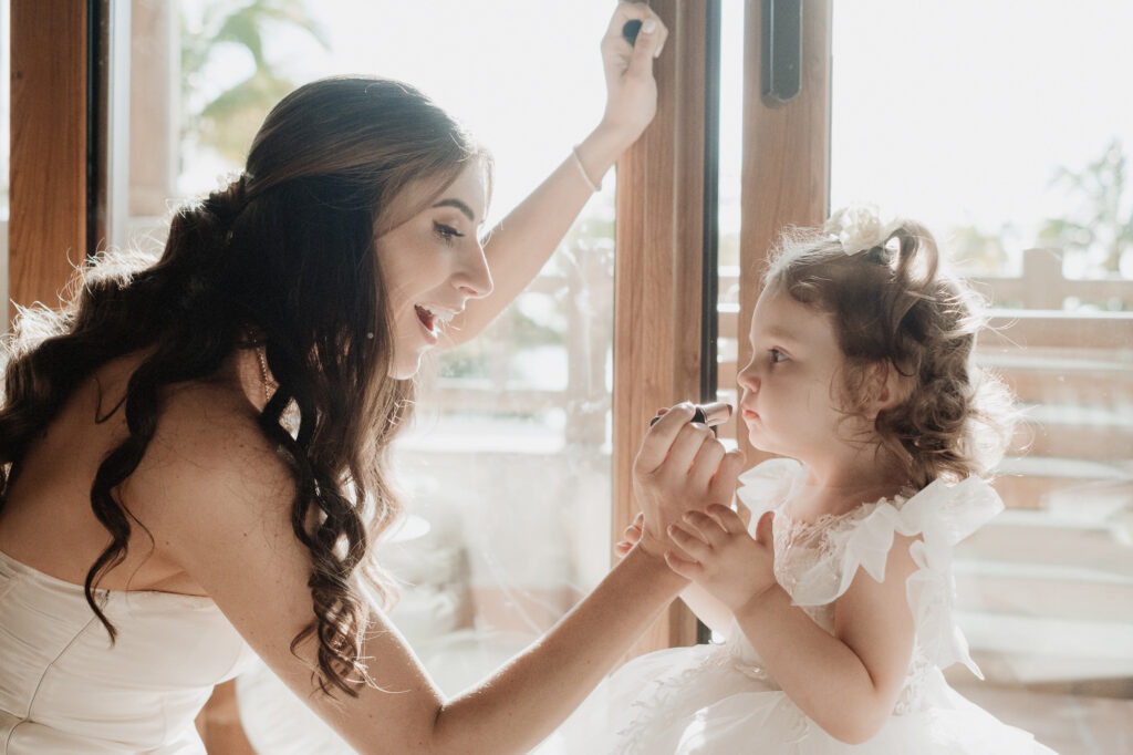 Bride applies lipstick to flower girl at St Regis Punta Mita elopement, both in white dresses