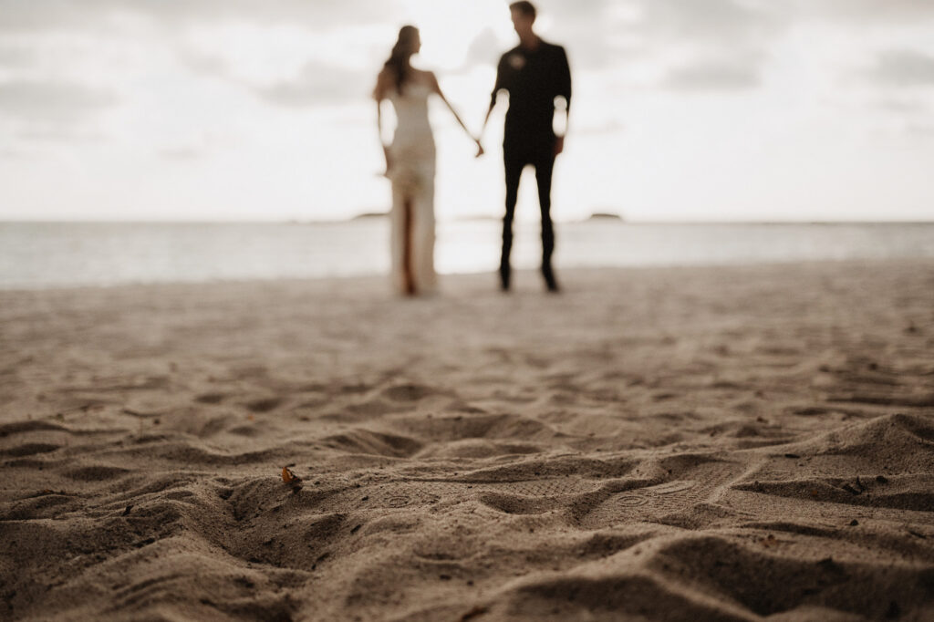 Elopement couple holding hands on beach at Punta Mita, blurred bokeh foreground, documentary style