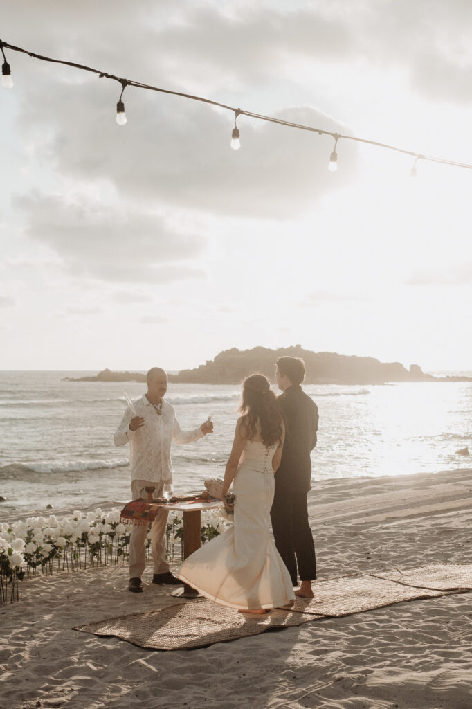 Beach elopement ceremony at sunset, St Regis Punta Mita, couple with officiant and white roses