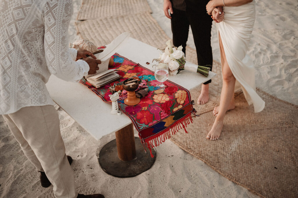 Elopement ceremony altar on the beach at St Regis Punta Mita with floral textile, bouquet, and bare feet in sand