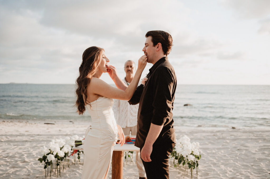 Couple feeding each other cake during beach elopement ceremony at St Regis Punta Mita, Mexico