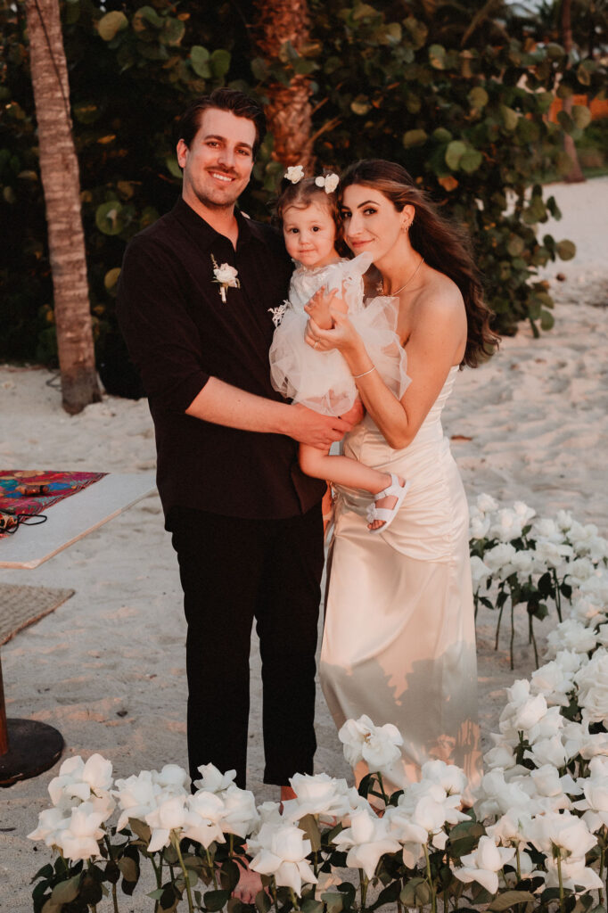 Couple with toddler daughter during beach elopement at St Regis Punta Mita, surrounded by white roses