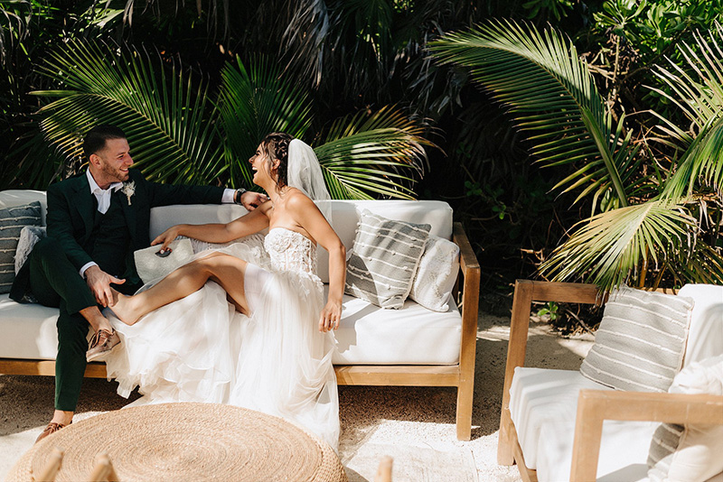 Bride and groom laughing on outdoor sofa at Papaya Playa Project, Tulum wedding reception