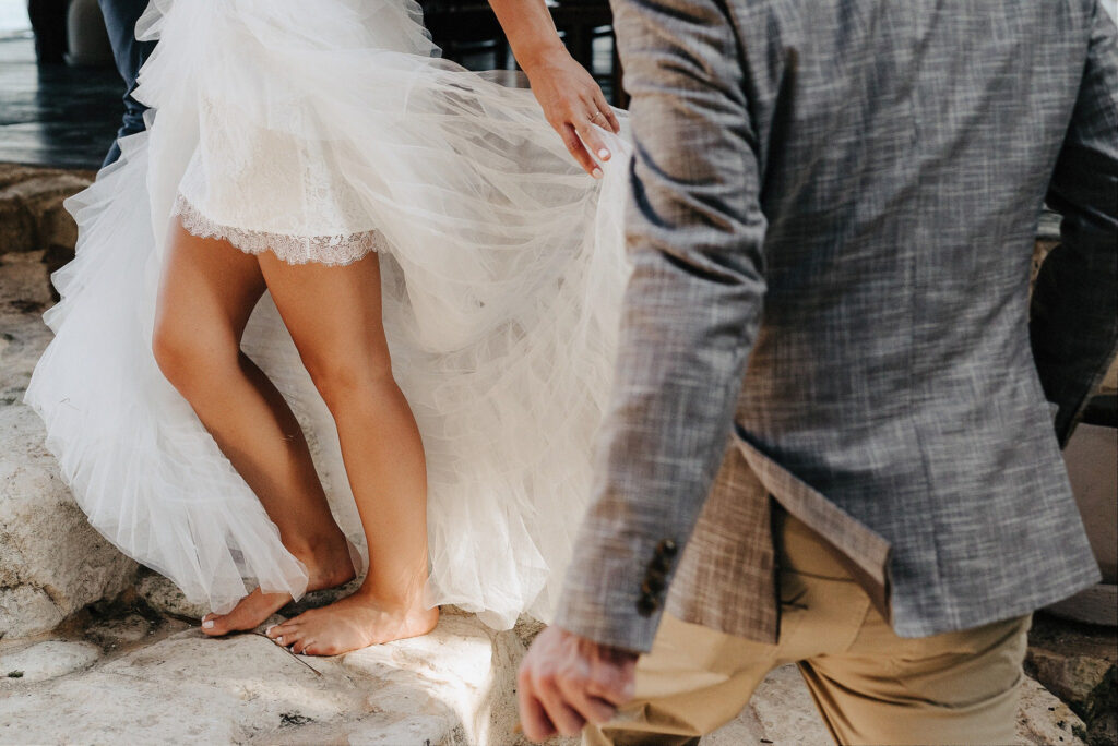 Bride lifting tulle wedding gown barefoot on rocks at Papaya Playa Project Tulum ceremony