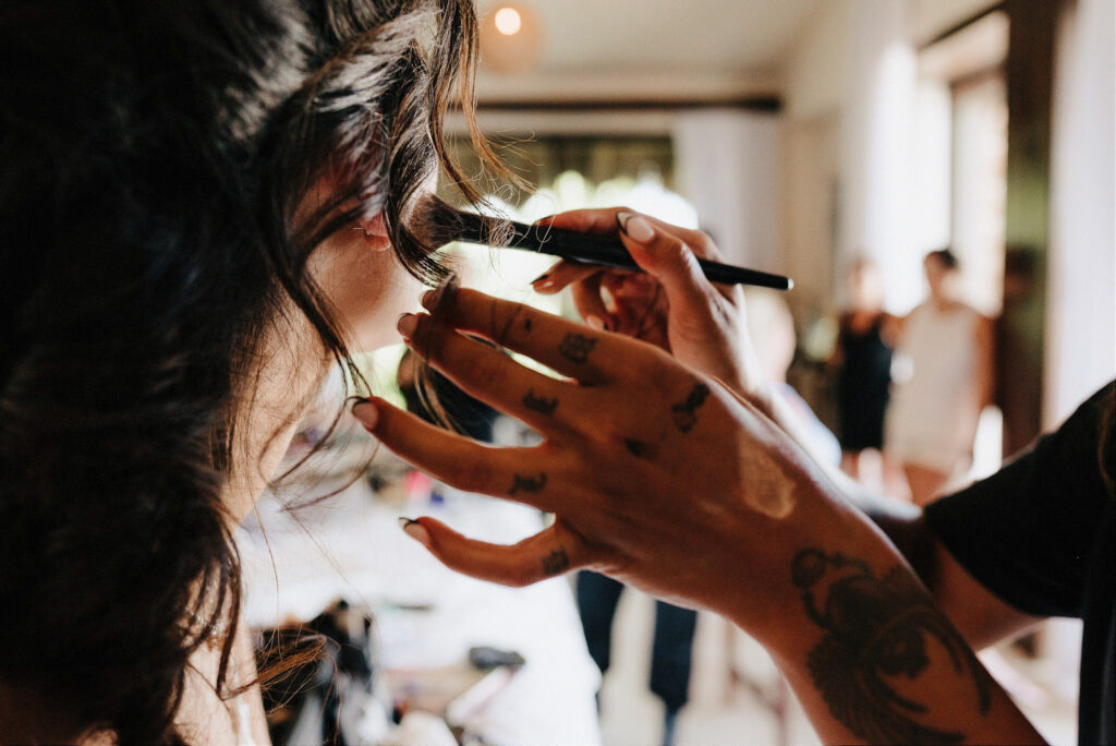 Tattooed makeup artist applying eyeshadow to bride before wedding at Papaya Playa Project, Tulum