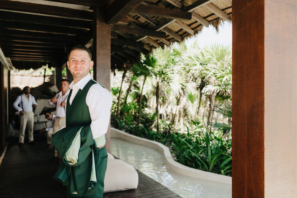 Groom in green suit holding jacket at Papaya Playa Project, Tulum wedding ceremony