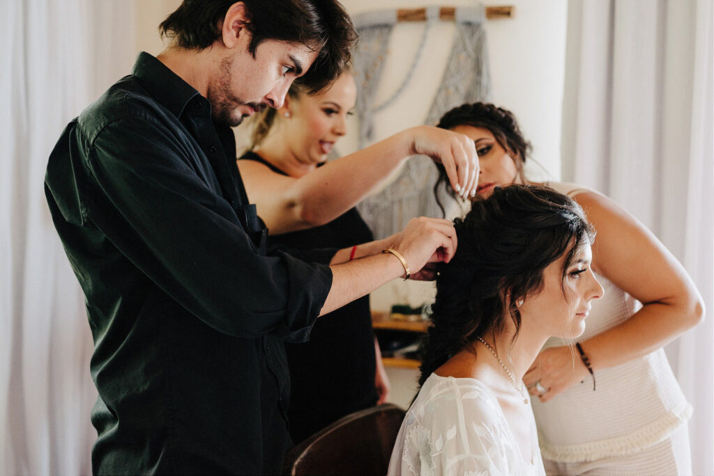 Bride getting hair styled by two artists before wedding ceremony at Papaya Playa Project, Tulum