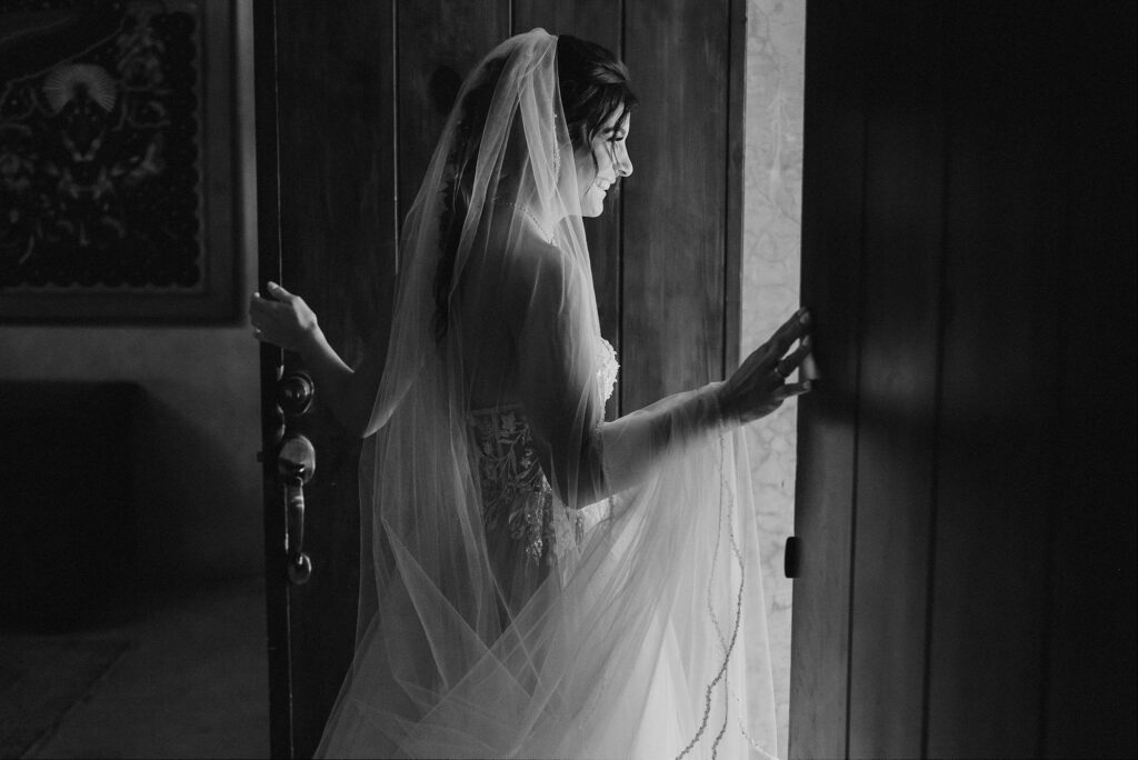 Bride in lace gown and veil opening wooden doors at Papaya Playa Project Tulum wedding ceremony