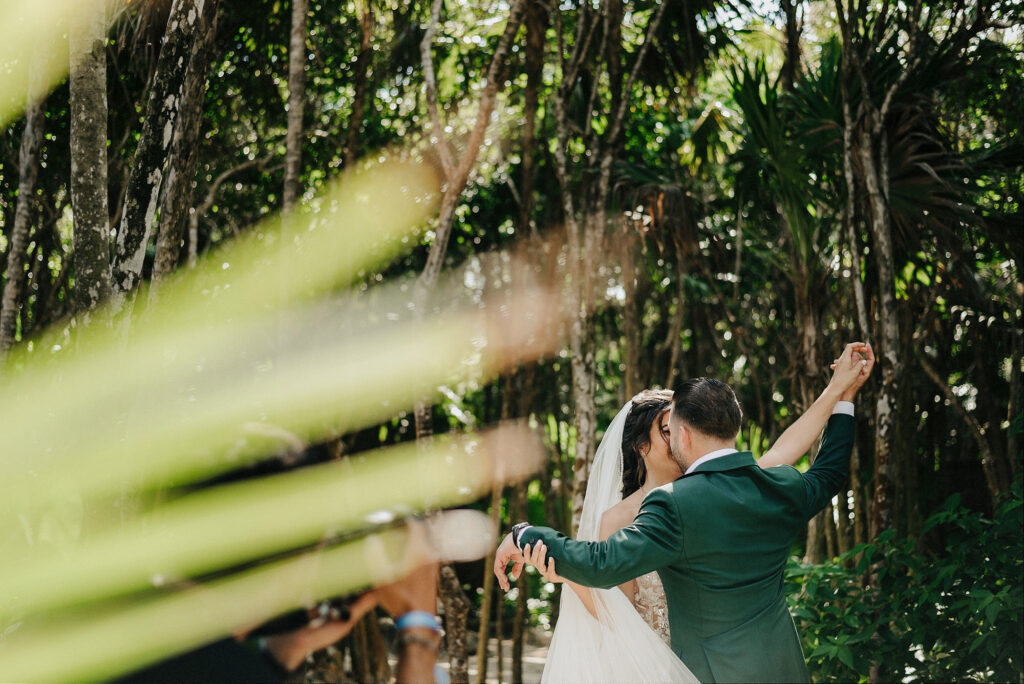 Bride and groom share first kiss surrounded by jungle trees at Papaya Playa Project Tulum wedding ceremony