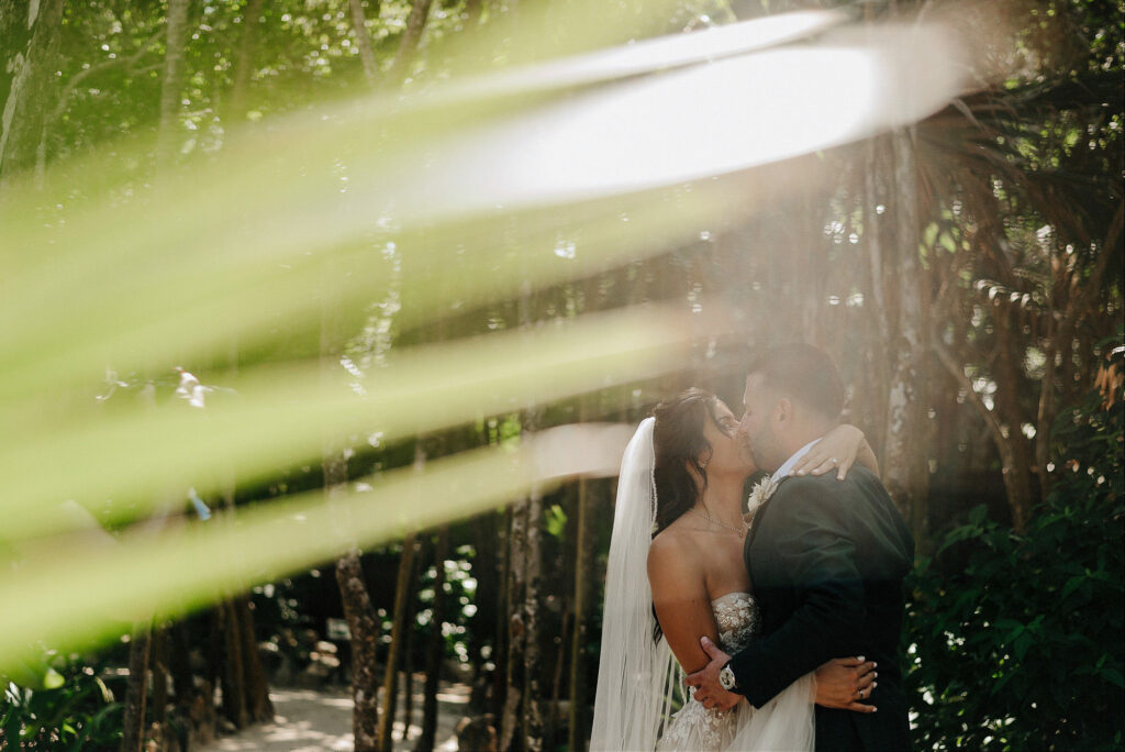 Bride and groom kissing in lush jungle setting at Papaya Playa Project Tulum wedding ceremony
