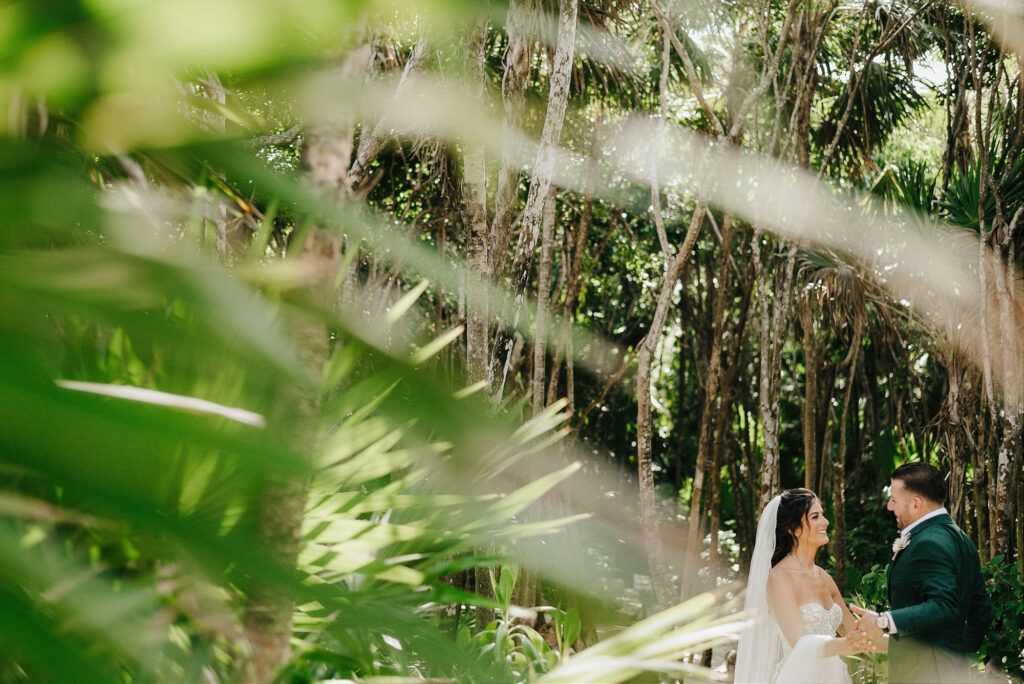 Bride and groom laughing in jungle at Papaya Playa Project Tulum wedding, shot through tropical foliage