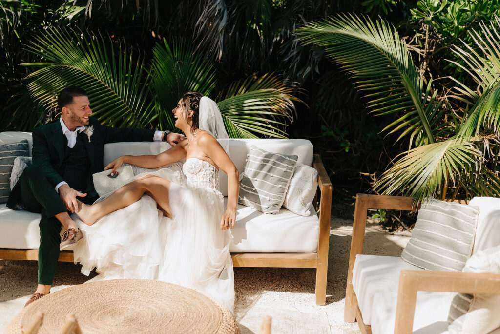 Bride and groom laughing together on outdoor sofa at Papaya Playa Project Tulum wedding reception