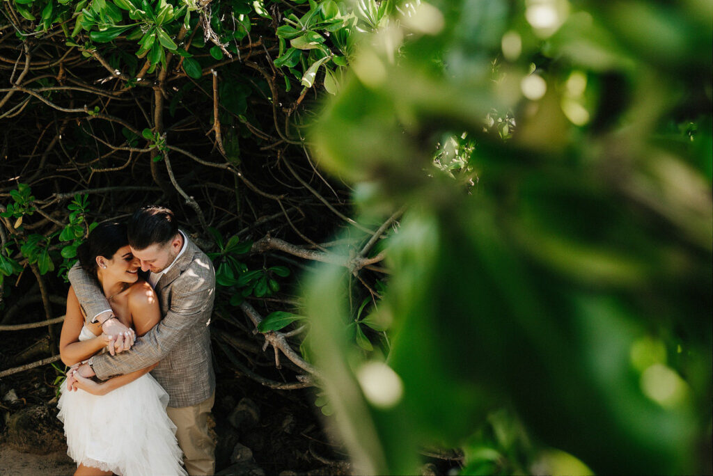 Bride and groom embracing among tropical trees at Papaya Playa Project Tulum wedding ceremony