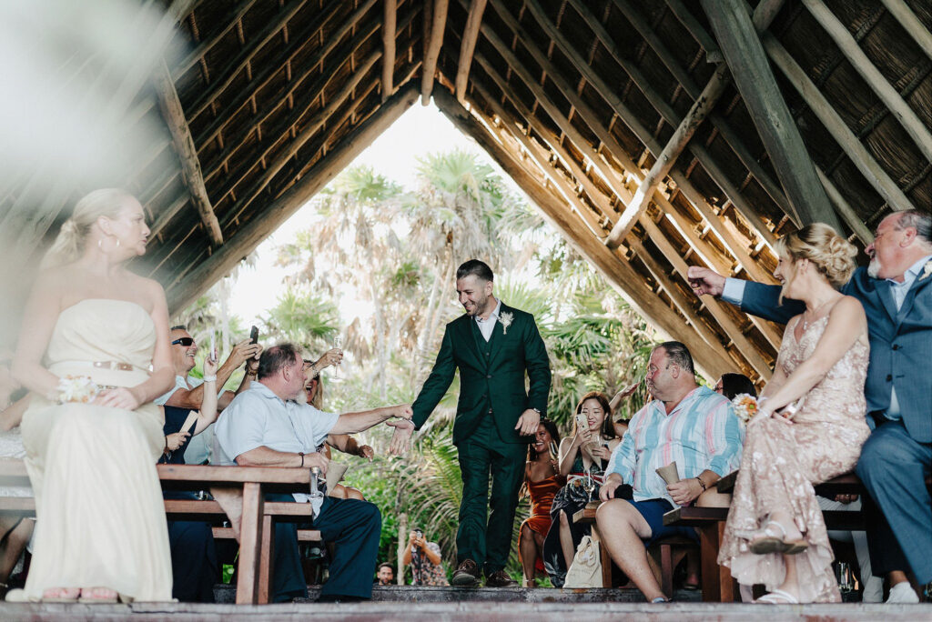 Groom walks down the aisle at Papaya Playa Project Tulum wedding ceremony, guests cheering