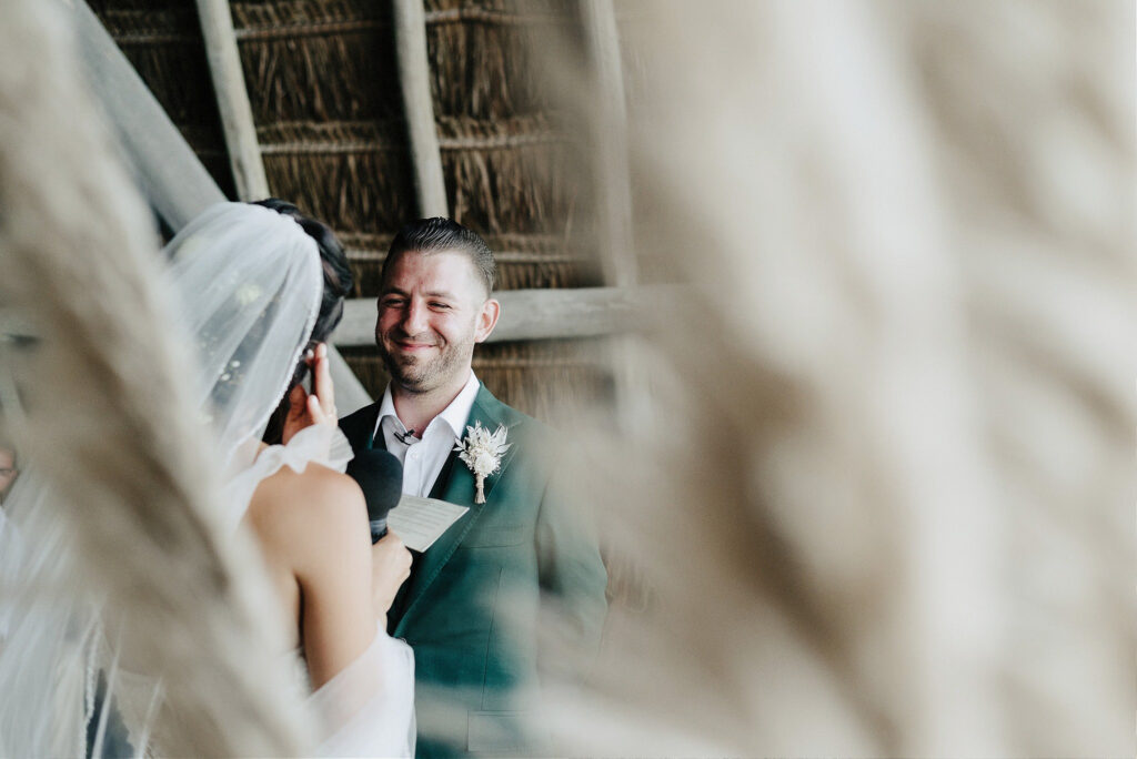Groom smiling at bride reading vows at Papaya Playa Project wedding ceremony, Tulum