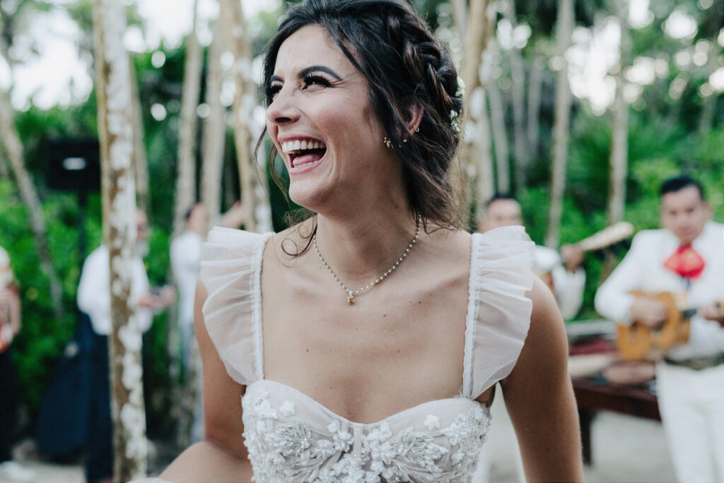 Bride laughing joyfully at outdoor wedding reception, Papaya Playa Project Tulum, mariachi band in background