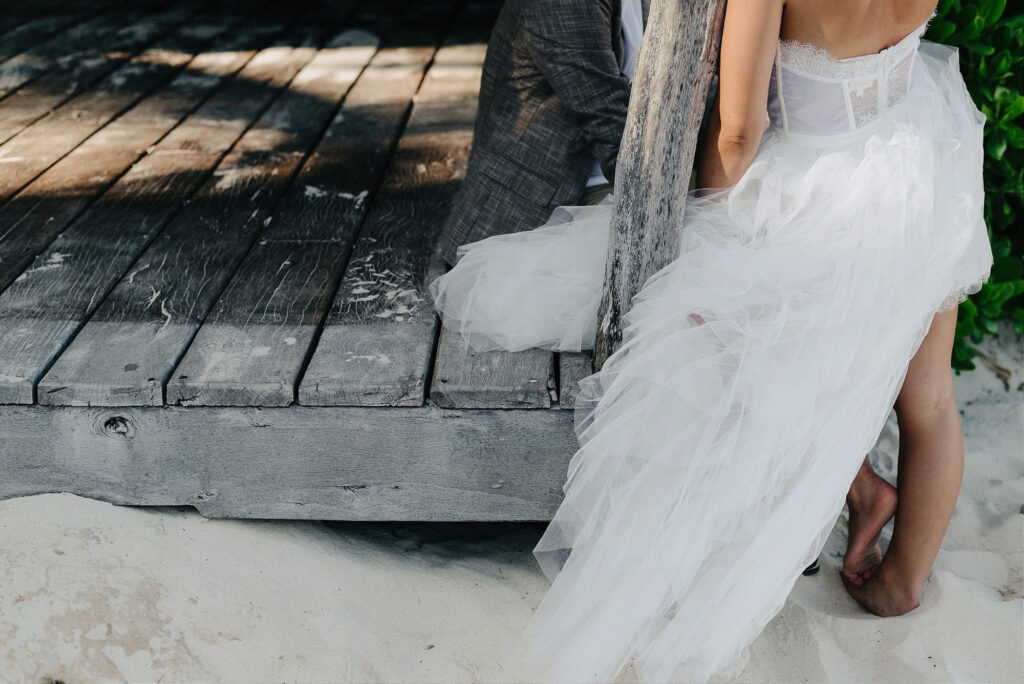 Bride in white tulle gown seated on wooden dock in white sand, Papaya Playa Project Tulum wedding