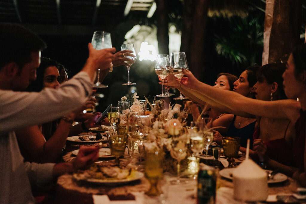 Wedding reception toast at Papaya Playa Project Tulum, guests raising wine glasses over floral table by Alex Obregón