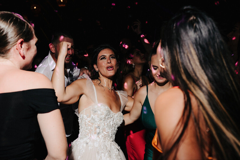 Bride dancing joyfully with guests at wedding reception, Papaya Playa Project Tulum, confetti falling
