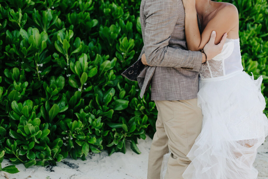 Bride and groom embracing on white sand beach at Papaya Playa Project, Tulum wedding ceremony
