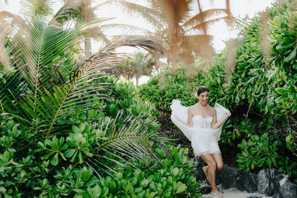 Bride laughing in white lace dress among tropical palms at Papaya Playa Project, Tulum wedding